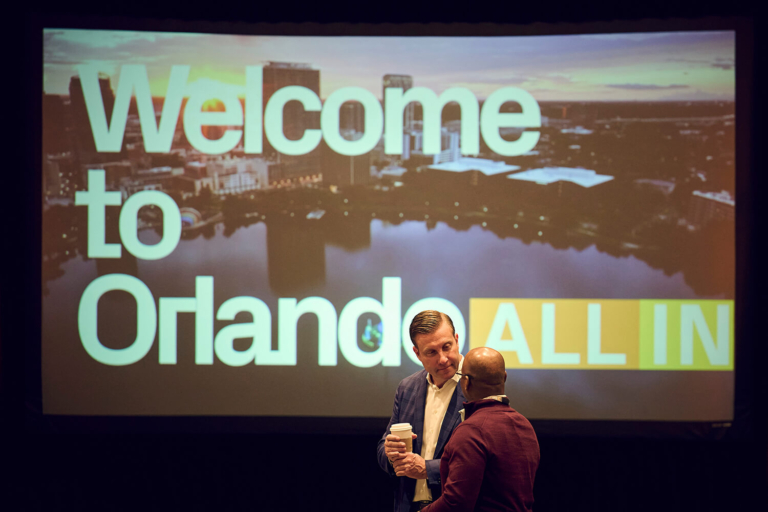 Speaker in front of a Welcome to Orlando slide at a corporate conference