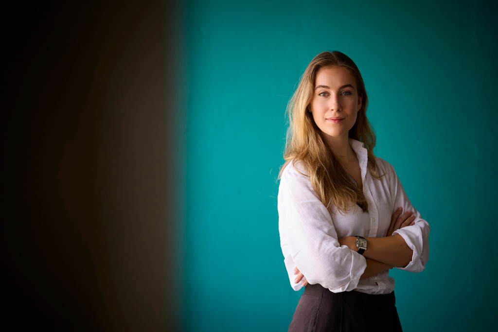 Professional headshot of a woman in a white shirt with arms crossed against a teal backdrop in Jupiter