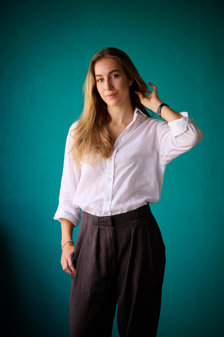 Personal branding portrait of a woman brushing her hair back against a teal backdrop
