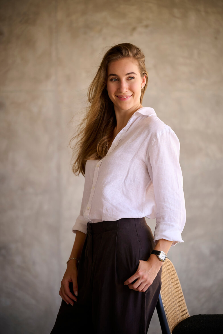 Professional portrait of a woman in a white shirt standing against a grey wall